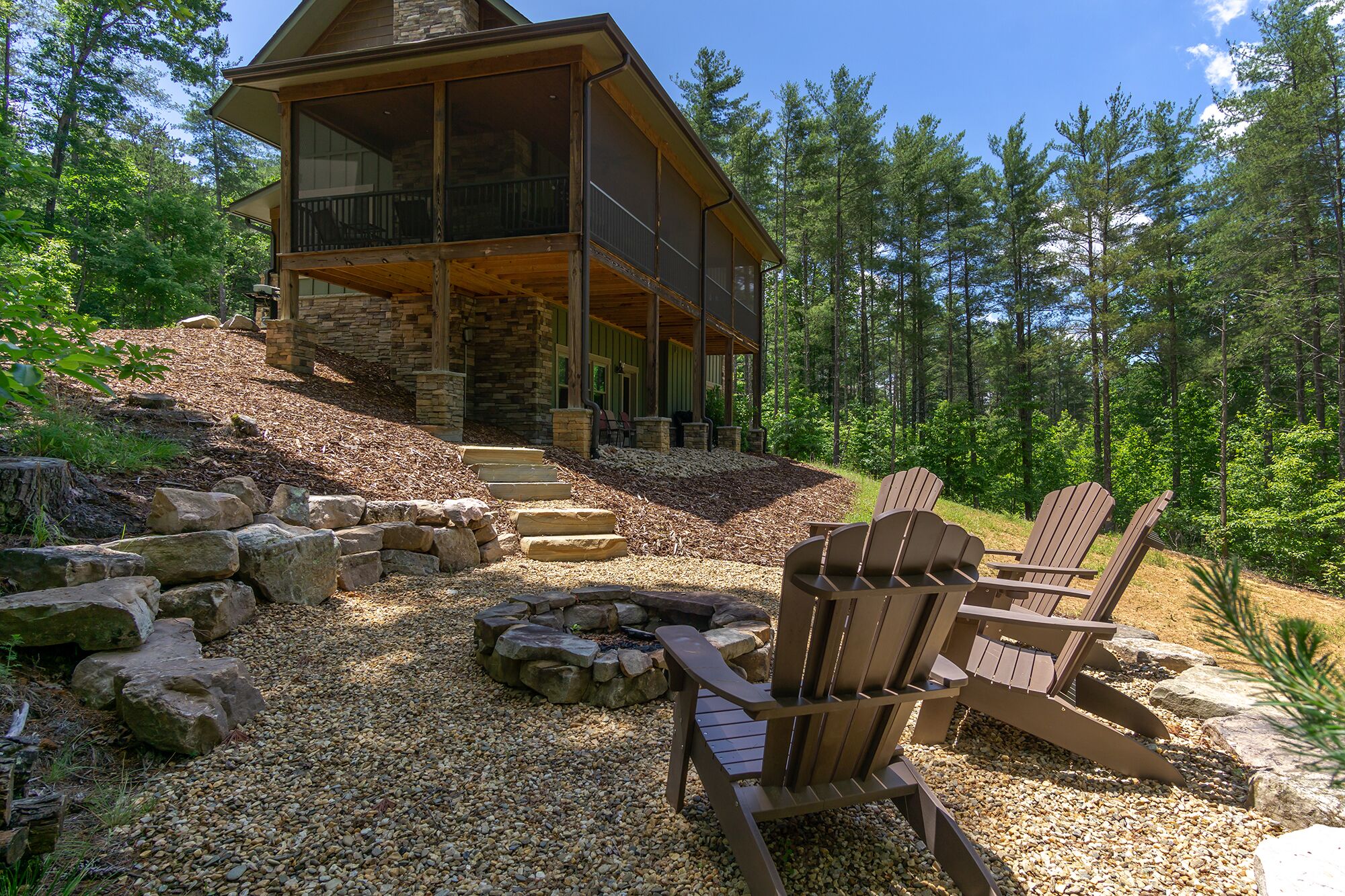 A cabin with a stone exterior, a covered porch, and a gravel patio with Adirondack chairs.