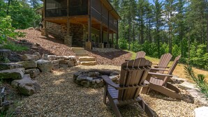 A cabin with a stone exterior, a covered porch, and a gravel patio with Adirondack chairs.