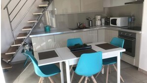 Ett modernt kök med ett vitt bord och turkosa stolar, en trappa i rostfritt stål och en mikrovågsugn.