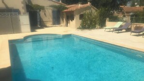 A rectangular swimming pool with a clear blue water surface, surrounded by a light-colored deck and a few lounge chairs. - House (Mimet)