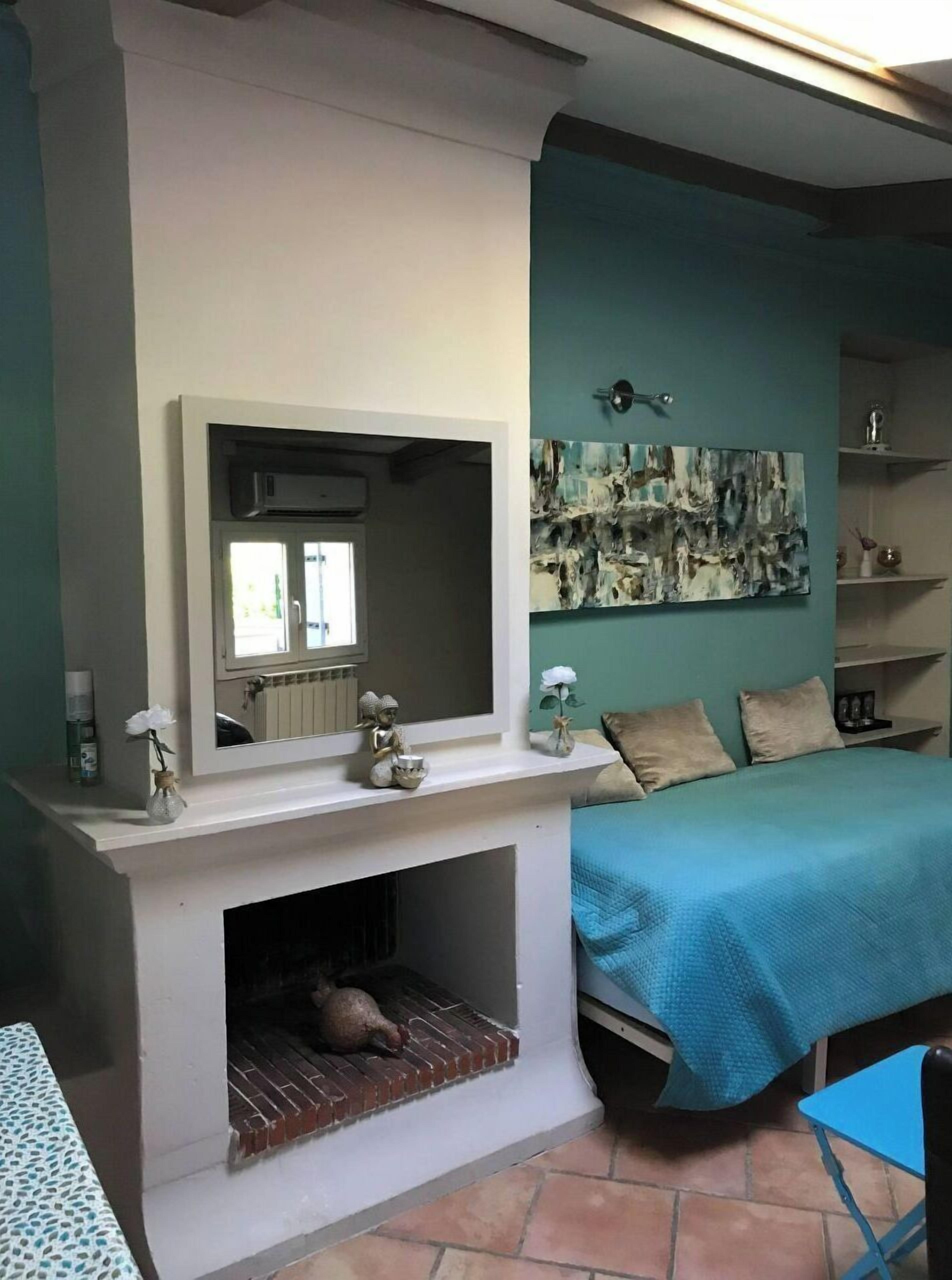Une chambre avec une cheminée, un lit recouvert d’une courtepointe bleue, un miroir fixé au mur et un tableau décoratif.