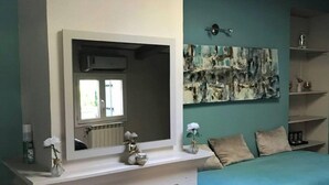 A bedroom with a fireplace, a bed with a blue bedspread, a wall-mounted mirror, and a decorative painting. - House (Mimet)