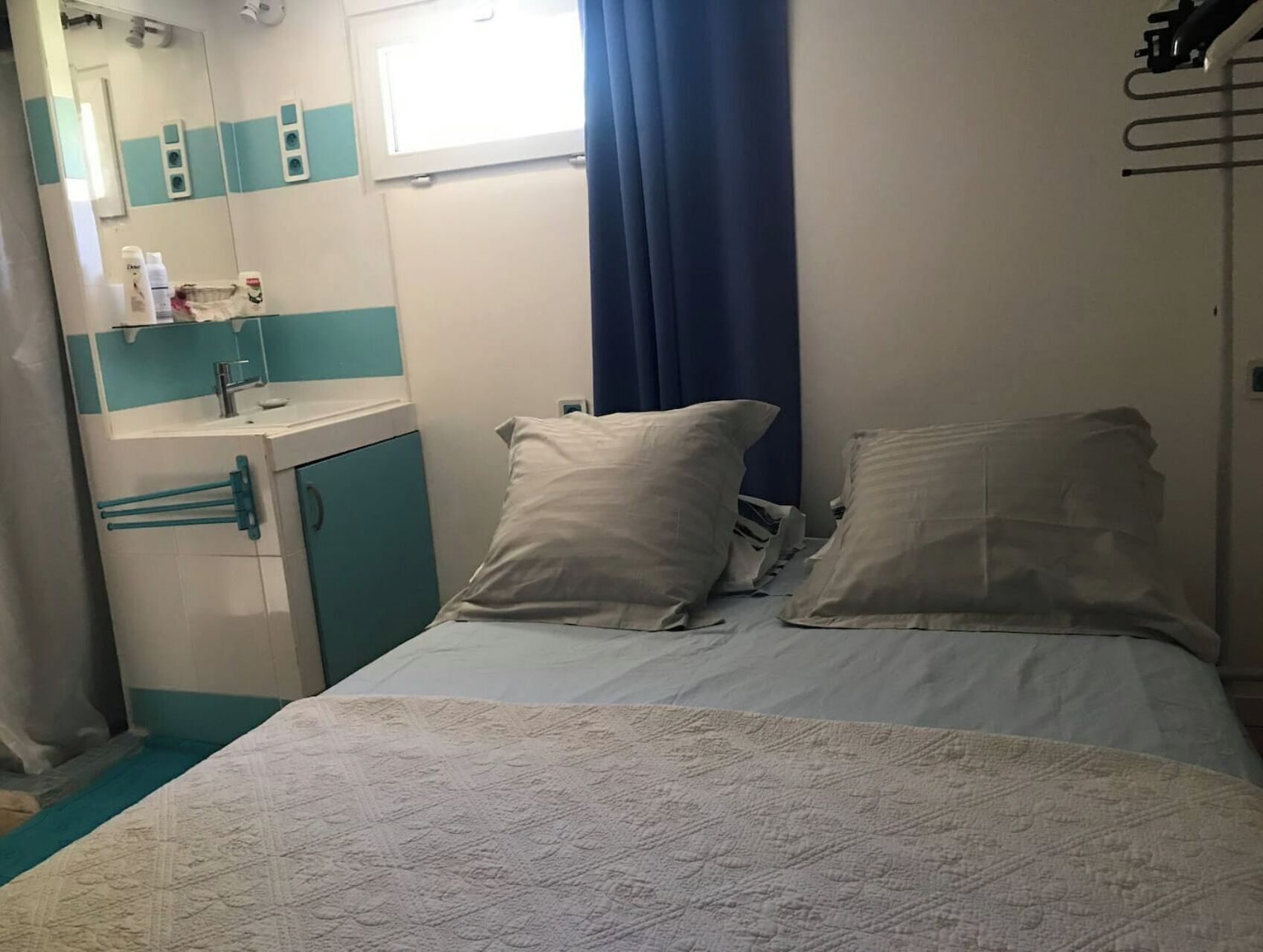 Een hotelkamer met een bed, kussens, een raam met gordijnen, een wastafel en een spiegel.