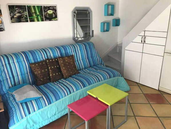 A room with a striped blue sofa, a small red and yellow table, a mirror, and a staircase.