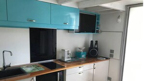 Une cuisine de taille réduite avec des meubles de couleur turquoise, un micro-ondes noir, une machine à café et un grille-pain.