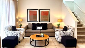 A living room with a sofa, two armchairs, a coffee table, and a staircase.