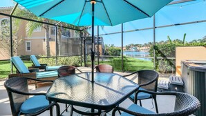 A covered patio with a glass table and chairs, overlooking a pool and greenery.