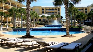 A resort pool area with palm trees, lounge chairs, and a fountain.