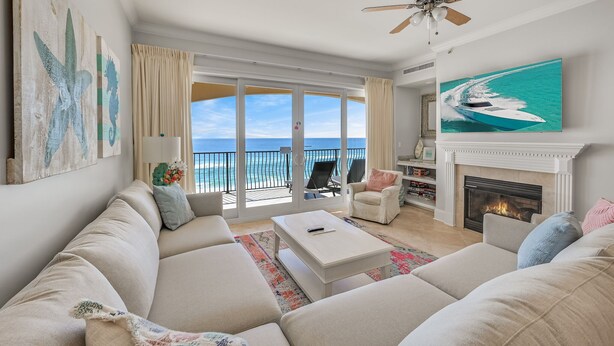 A spacious living room with a large sofa, a fireplace, and a balcony with a view of the ocean.
