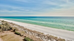 A beach with a clear sky, a sandy shore, and a road running parallel to the beach.