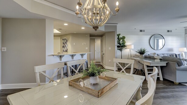 A dining area with a chandelier, a dining table, and chairs. There is a kitchen in the background with a countertop and cabinets. - 3106 Windsor Court S - Amazing Oceanfront Villa in Palmetto Dunes! (Hilton Head Island)