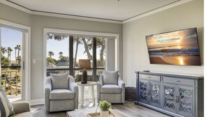 A living room with two patterned armchairs, a coffee table with a tray and plant, a cabinet with decorative cutouts, and a TV displaying 'VACATIONCOMPANY'. - 3106 Windsor Court S - Amazing Oceanfront Villa in Palmetto Dunes! (Hilton Head Island)