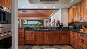 A modern kitchen with wooden cabinets, a granite countertop, and stainless steel appliances. - Hualalai Waiulu Villa 133B ~ Updated, Spacious with Great Views! (Kailua-Kona)