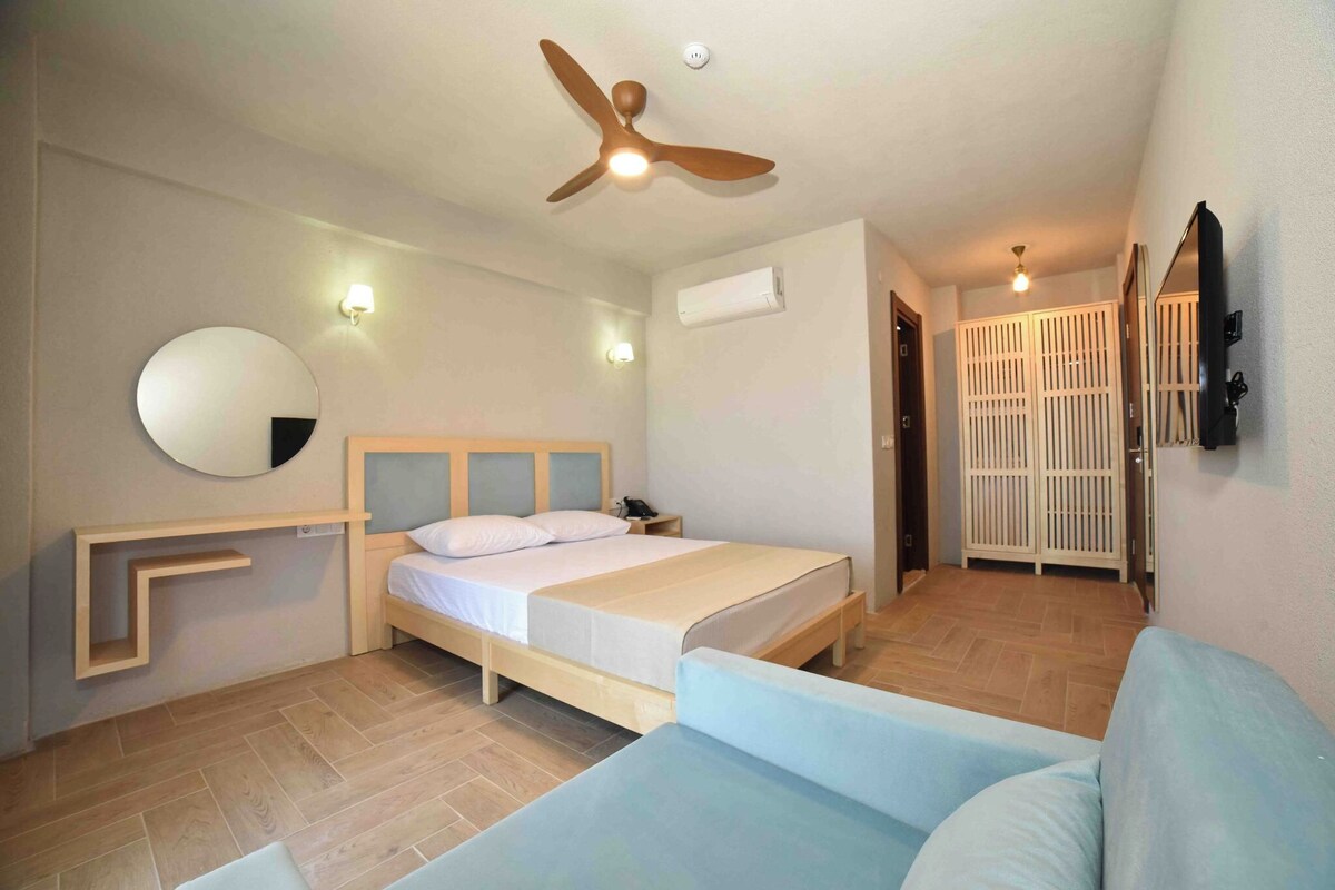 Un dormitorio con cama, ventilador de techo, mesita de noche, espejo y armario.