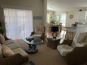 Una sala de estar con muebles de mimbre, una mesa de centro de vidrio y una zona de comedor con una mesa y sillas.