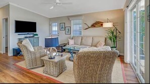 A spacious living room with a large flat-screen TV, comfortable seating, a ceiling fan, and a large window providing natural light. - Saint James hidden gem. 3/2 canal front home with 3 kayaks.  (Saint James City)