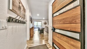 A hallway with a wooden door, a coat rack, and a view into a room with a pool table.