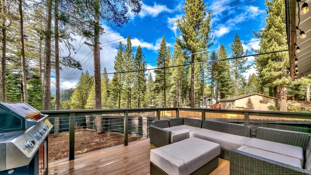 A deck with a grill, wicker furniture, and a view of tall trees.