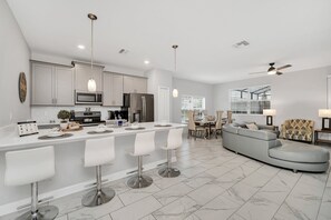 A modern kitchen with a central island, bar stools, and a dining area with a sofa and table. - Private Splash Pool • Waterpark • Lazy River • Golf • Near Disney • Gated Resort (Davenport)
