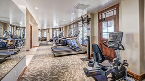 Een fitnessruimte met loopbanden, elliptische trainers en hometrainers, voorzien van vloerbedekking en grote ramen.