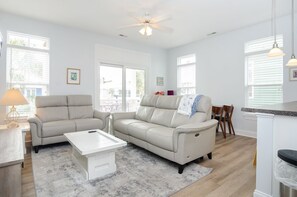 Ein geräumiges Wohnzimmer mit einem beigen Sofa, einem weißen Couchtisch und einem Deckenventilator.