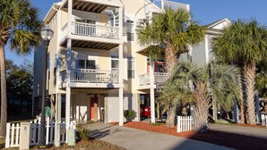 A multi-story residential building with balconies, a garage, and palm trees. - 3 BR duplex w Rooftop sundeck and ocean views! (Carolina Beach)