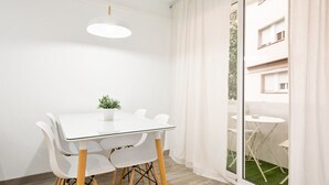 A modern room with a glass table and white chairs, a potted plant, and a view of a building through a glass door. - GE1 (Barcelona)