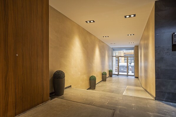 A modern hallway with a wooden wall on the left, a dark wall on the right, and a glass door at the end. - GE6 (Barcelona)