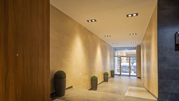 A modern hotel corridor with wooden walls, recessed lighting, and potted plants. - G14 (Barcelona)