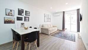 A modern living room with a dining area, featuring a sofa, a coffee table, and a dining table with chairs. There are several framed pictures on the walls. - G14 (Barcelona)