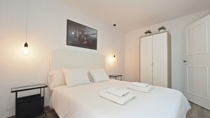 A neatly made bed with white linens and towels, a black side table, a wall-mounted picture, and a white wardrobe. - G14 (Barcelona)