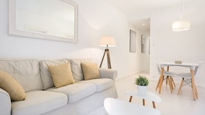 Un salon moderne avec un canapé, une petite table agrémentée d’une plante, et un coin repas comprenant une table et des chaises.