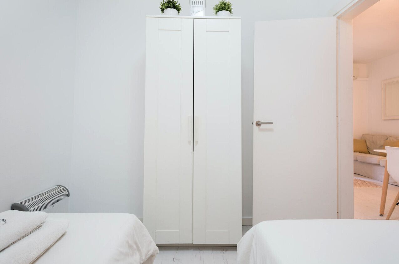 Ett hotellrum med en vit garderob, en säng, ett element och utsikt över ett vardagsrum med en soffa och en växt.