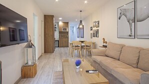 Ett modernt vardagsrum med en soffa, ett soffbord och en tv. Längre bak i rummet finns ett kök med en matplats.