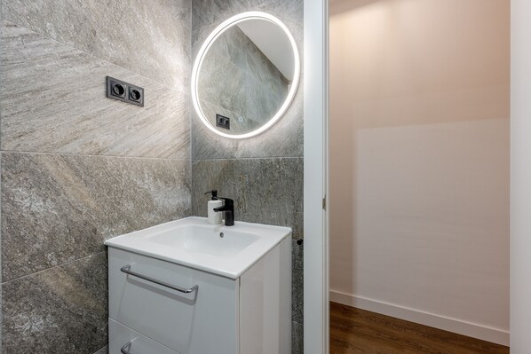 Une salle de bain avec un lavabo blanc, un miroir avec un éclairage intégré et un mur en marbre.