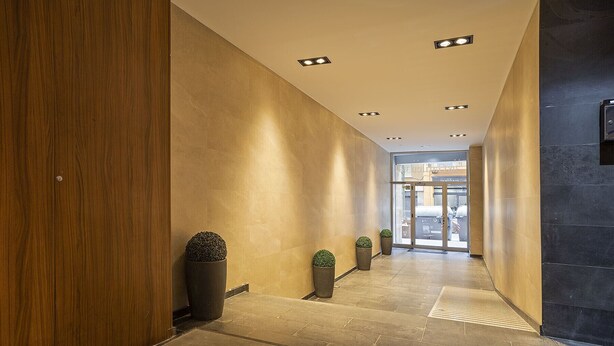 A modern hallway with a wooden wall on the left, a dark wall on the right, and a glass door at the end. - G25 (Barcelona)