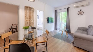 A modern living room with a glass dining table, wooden chairs, a grey sofa, and a TV mounted on the wall. - G25 (Barcelona)