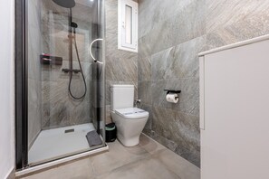 A modern bathroom with a glass-enclosed shower, a toilet, and a marble-tiled wall. - G25 (Barcelona)