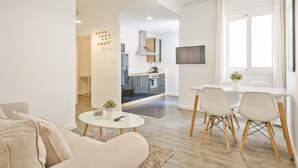 Un salon moderne avec un canapé, une table basse et un coin repas avec des chaises. On aperçoit une cuisine au fond.