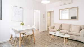 Un salon moderne avec un canapé blanc, une table à manger avec des chaises, une table basse, un tableau encadré au mur et un grand miroir.
