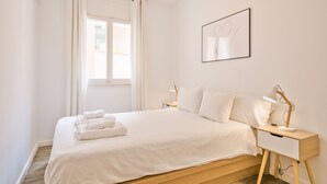 Un lit bien fait, avec du linge de lit blanc et un ensemble de serviettes, une table de chevet avec une lampe et un tableau encadré au mur.