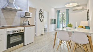 A modern kitchen with a built-in oven, microwave, and stove. There is a dining area with a glass table and white chairs. - G33 (Barcelona)