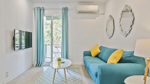 A modern living room with a teal sofa, yellow cushions, a glass coffee table, and a TV on the wall. - G33 (Barcelona)