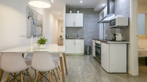 A modern kitchen with white cabinets, a microwave, and a small refrigerator. There is a dining table with chairs and a hanging light fixture. - G33 (Barcelona)