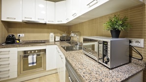 A modern kitchen with white cabinets, a built-in oven, a microwave, and a coffee maker.