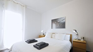 A neatly made bed with two folded towels, a bedside lamp, and a nightstand with a lamp.