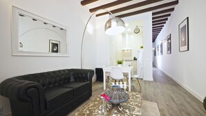 Ein modernes Wohnzimmer mit einem schwarzen Ledersofa, einem Couchtisch mit Dekoration, einem großen Spiegel und einem Essbereich mit weißem Tisch und Stühlen.