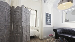 Ein Schlafzimmer mit einem Bett, einer schwarzen Ledersofa, einem dekorativen Raumteiler, einem Spiegel und einem Poster.
