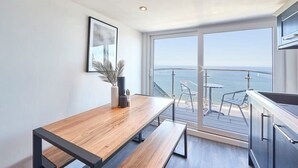 A modern kitchen with a wooden table, bench, and a view of the sea through large windows. - Host & Stay | Penthouse Pier View (Whitby)