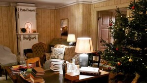 A cozy living room with a fireplace, a Christmas tree, and a dining area with books and a lamp.